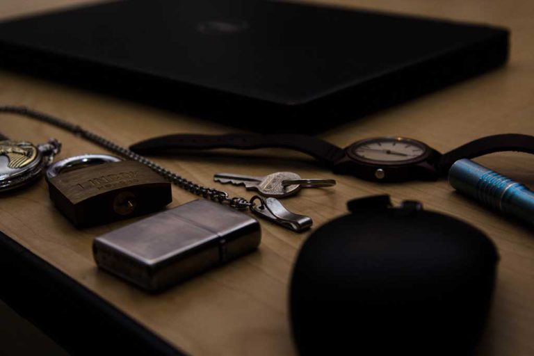 keys, lighter, pocket watch, watch, pen on a desktop in dim light